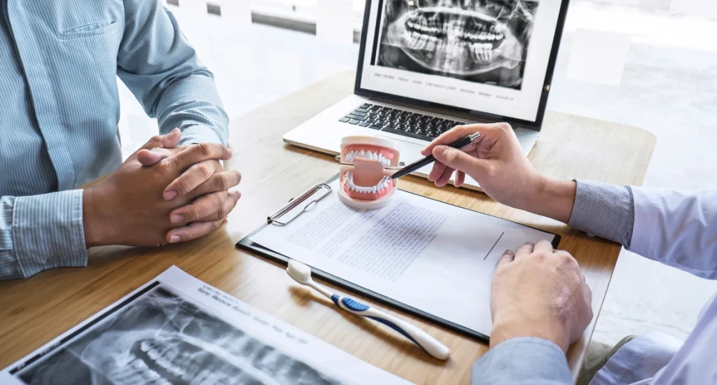 Dentist using dental model and X-ray images to explain treatment plan to a patient during consultation at a dental clinic.