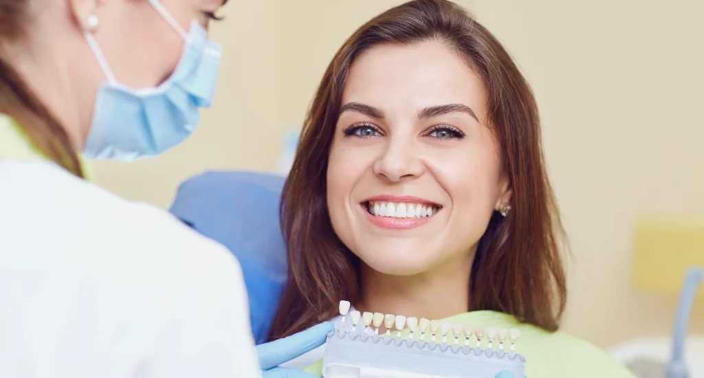 Happy woman at dental clinic selecting tooth shade for cosmetic whitening procedure with the help of a dentist.