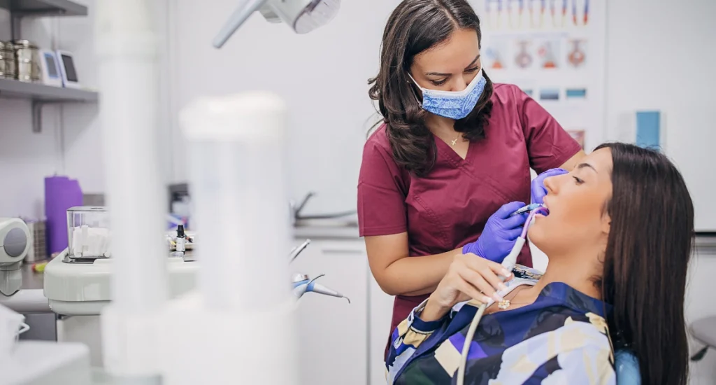 A dental professional wearing gloves and a mask treating a female patient in a modern dental clinic using professional dental tools.